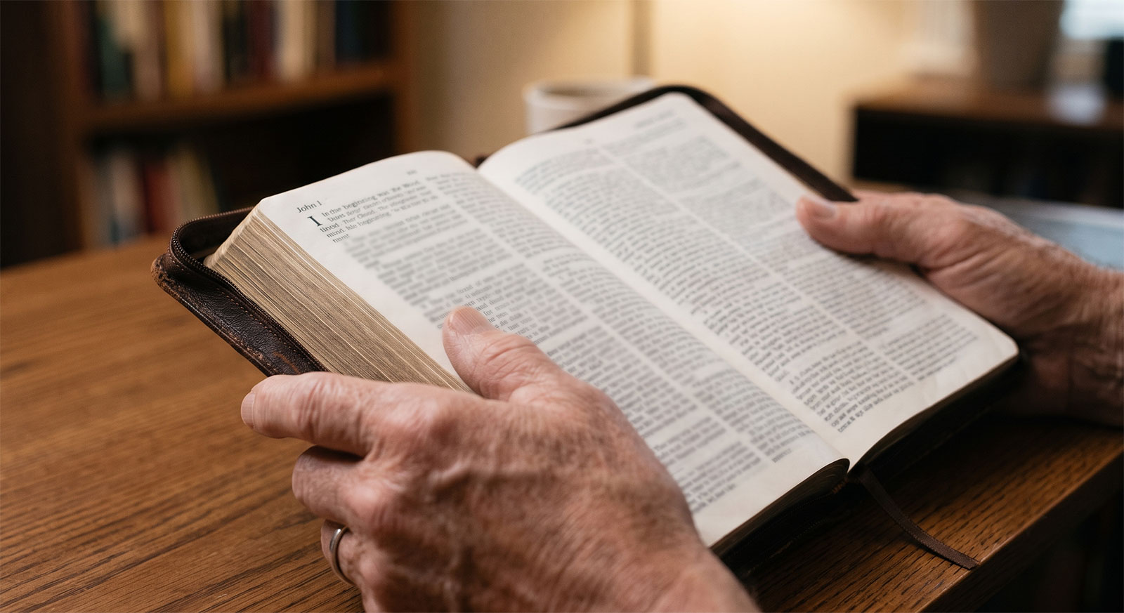 Open Bible held in both hands at a wooden desk